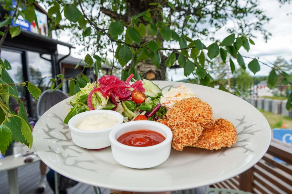 Crispy chicken with salad served on the terrace of Café Ensilumi, with a birch tree and summer scenery in the background.