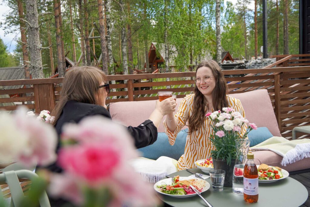 Visitors enjoying a summer lunch on the sunny terrace of Café Ensilumi in Santa Claus Village, Rovaniemi.